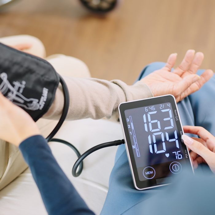 Close up woman caregiver nurse wearing blue scrubs checks blood pressure monitor and heart rate monitor with digital pressure gauge to elderly woman retirement sitting on bed in bedroom,healthcare setting medical health care plan