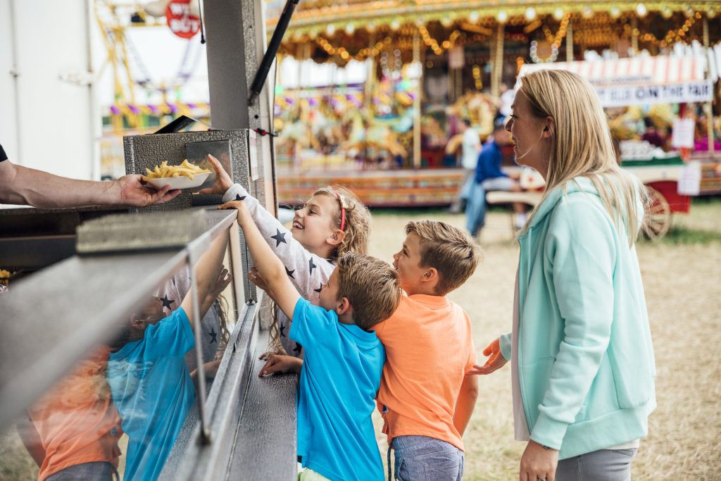 Children with their mother getting some food at a fairground. They are buying french fries at a fast food van.