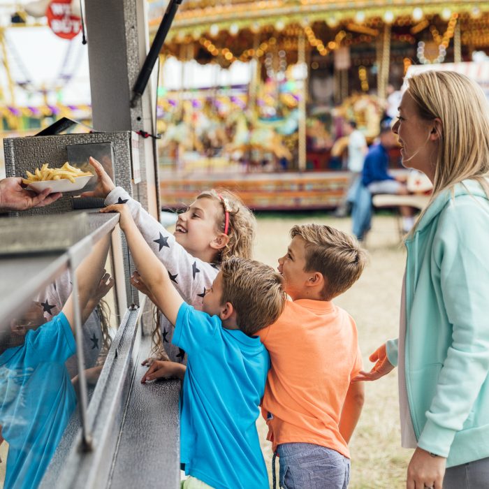 Children with their mother getting some food at a fairground. They are buying french fries at a fast food van.